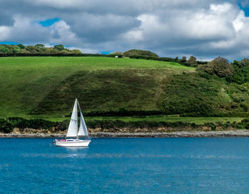 Sailboat in sea against cloudy sky