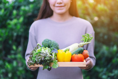 Midsection of smiling woman holding vegetables on tray