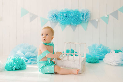 A one-year-old boy in a summer suit with a butterfly sits on the photo zone of his birthday 