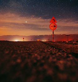 Road sign on field against sky at sunset