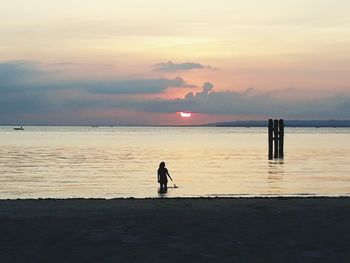 Silhouette woman standing on beach against sky during sunset