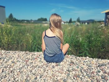 Rear view of woman sitting on pebbles