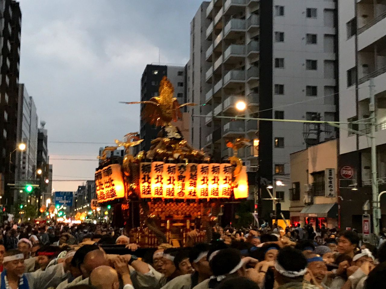 CROWD AT ILLUMINATED CITY AGAINST SKY