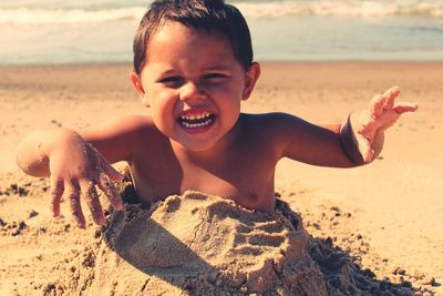 Portrait of shirtless boy enjoying in sand at beach on sunny day