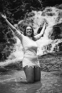 Portrait of young woman with arms raised standing in water