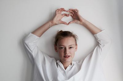 Portrait of woman making heart shape with hands against white wall