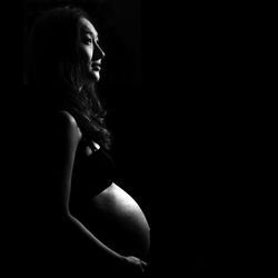 Pregnant woman standing against black background