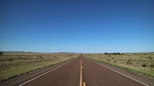 Road passing through land against clear blue sky