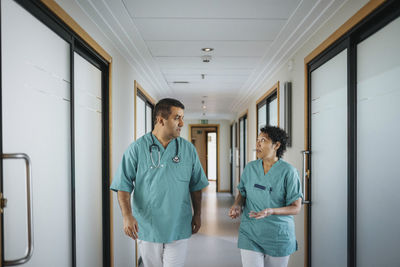 Multiracial male and female healthcare workers discussing while walking in corridor of hospital