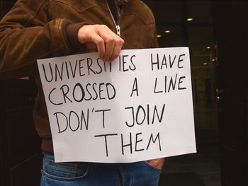 Midsection of protestor holding paper with text