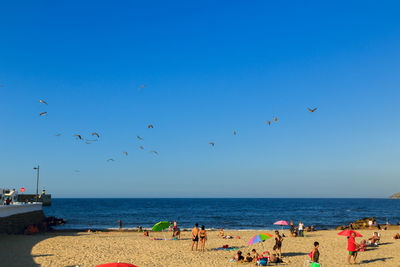 People at beach against clear blue sky