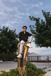 Young transgender man with glasses posing on a log outdoors.