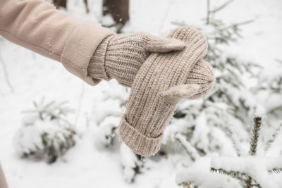 Knitted beige mitten in a woman's hand near the snow