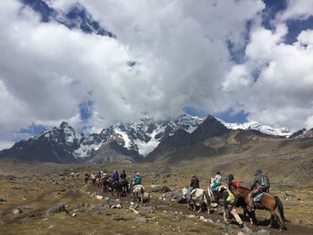 People horseback riding on snowcapped mountains against sky