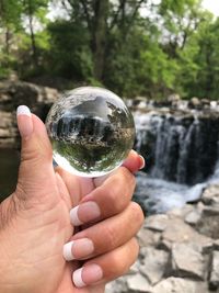 Cropped image of hand holding crystal ball on rock