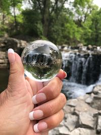 Cropped hand of woman holding crystal ball against waterfall