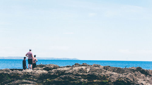 Rear view of three men standing on coast