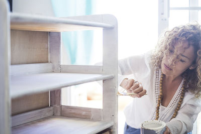 Woman painting cabinet at home