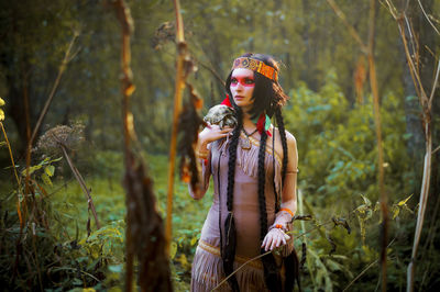 Young woman in traditional clothing carrying tortoise in forest