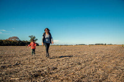 Grandmother with grandson walking on land against blue sky