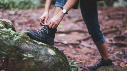 Closeup image of a woman hiker tying shoelaces and getting ready for trekking in the forest