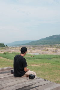 Rear view of man sitting on landscape against mountain