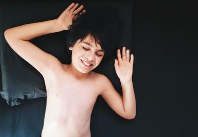Directly above shot of happy shirtless boy resting on bed