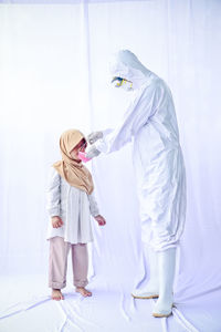 Full length of man wearing protective suit and mask to cute girl against white background