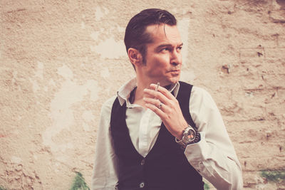 Man smoking will standing against wall