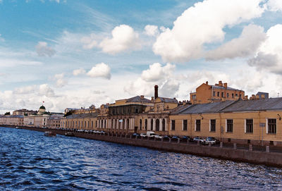 Buildings by river against cloudy sky