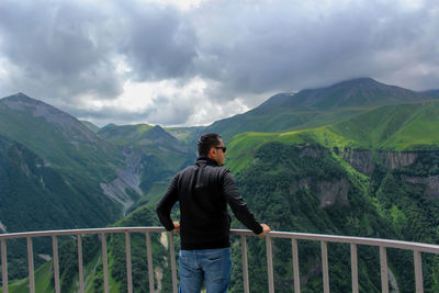 Rear view of man standing by railing against mountains