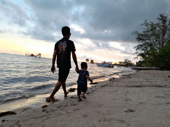 Rear view of children on beach against sky