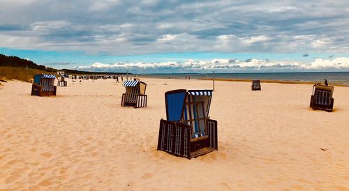 Hooded chairs at beach against cloudy sky