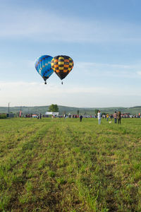 People looking at hot air balloons flying over landscape against sky