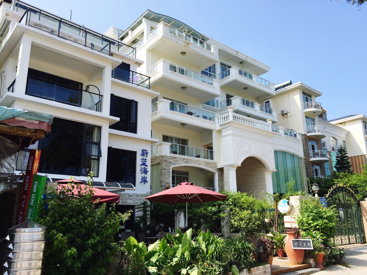 building exterior, architecture, built structure, clear sky, residential building, residential structure, house, low angle view, building, city, potted plant, window, balcony, tree, blue, day, sunlight, outdoors, roof, sky