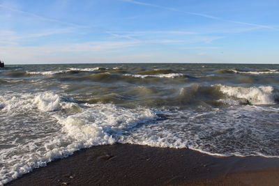 Waves rushing towards shore against sky