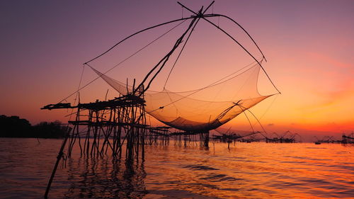 Silhouette cranes against sky at sunset