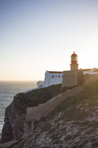 Lighthouse by sea against clear sky during sunset