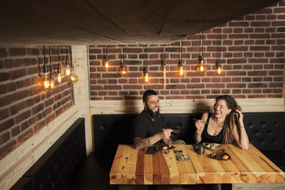 Loving couple eating appetizing sushi while sitting at wooden table in japanese restaurant