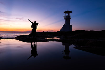 Silhouette man standing on rock by sea against sky during sunset