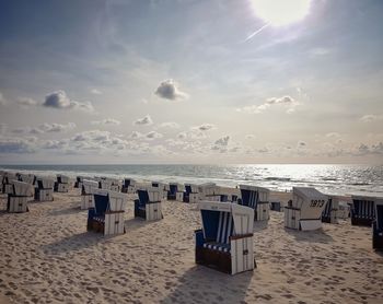 Hooded chairs on beach against sky