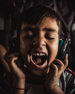 Close-up of boy with mouth open listening music through headphones