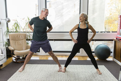 Cheerful couple exercising together against windows at home