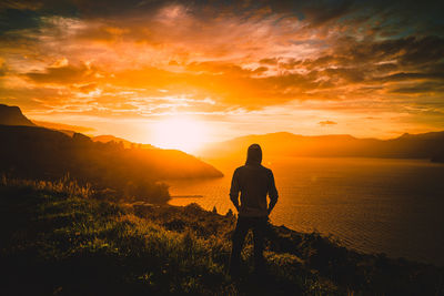 Rear view of man standing on mountain against sea during sunset