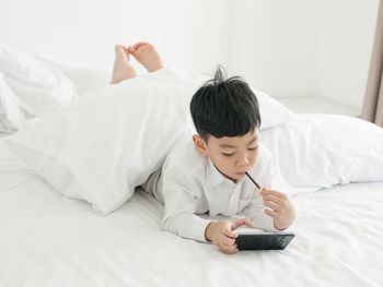 High angle view of cute boy using phone while lying on bed at home