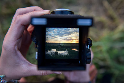 Cropped hands of woman photographing swamp against cloudy sky