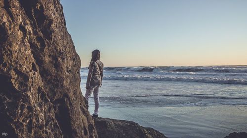 Woman standing on rock by sea against clear sky