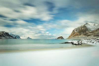 Scenic view of sea by snowcapped mountain against sky