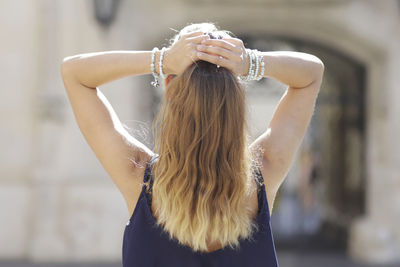 Rear view of woman tying hair while standing against built structure