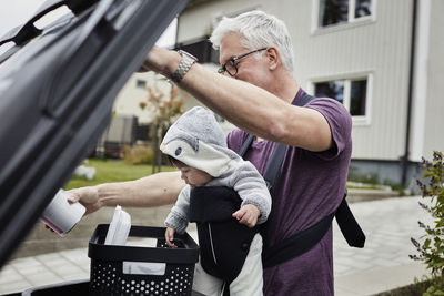 Smiling mature man with baby putting rubbish into bin